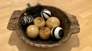 4 gedrechselte Holzkugeln zusammen mit 3 schwarz-weißen Christbaumkugeln in einer Holzschale